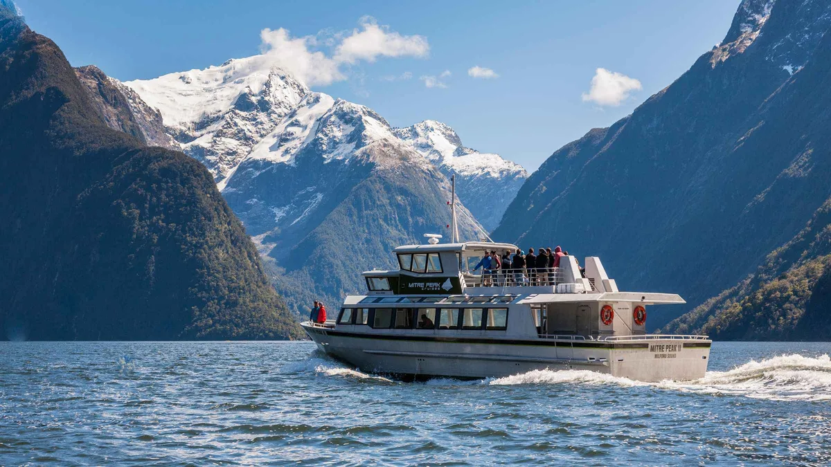 Small boat passing a waterfall under Mitre Peak on a Milford Sound boat tour in Fiordland, New Zealand