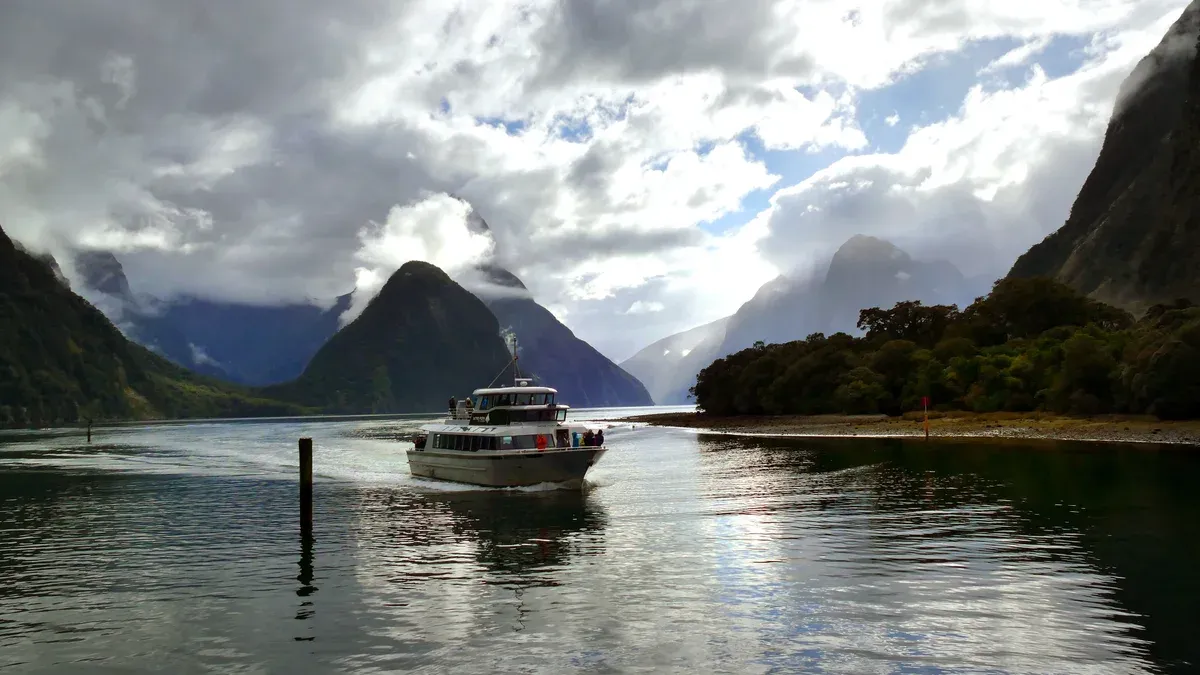 A small cruise boat on calm water with Mitre Peak and cloud behind on a Milford Sound cruise